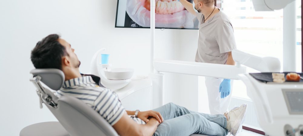 dentist-discussing-with-laying-patient-showing-the-image-of-his-teeth-on-the-screen dentist-discussing-with-laying-patient-showing-the-image-of-his-teeth-on-the-screen